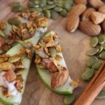A wooden cutting board topped with sliced apples and nuts.
