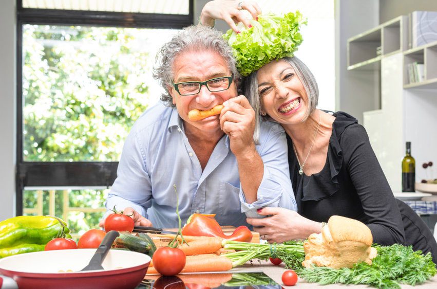 A man and woman sitting at the table with vegetables on it.