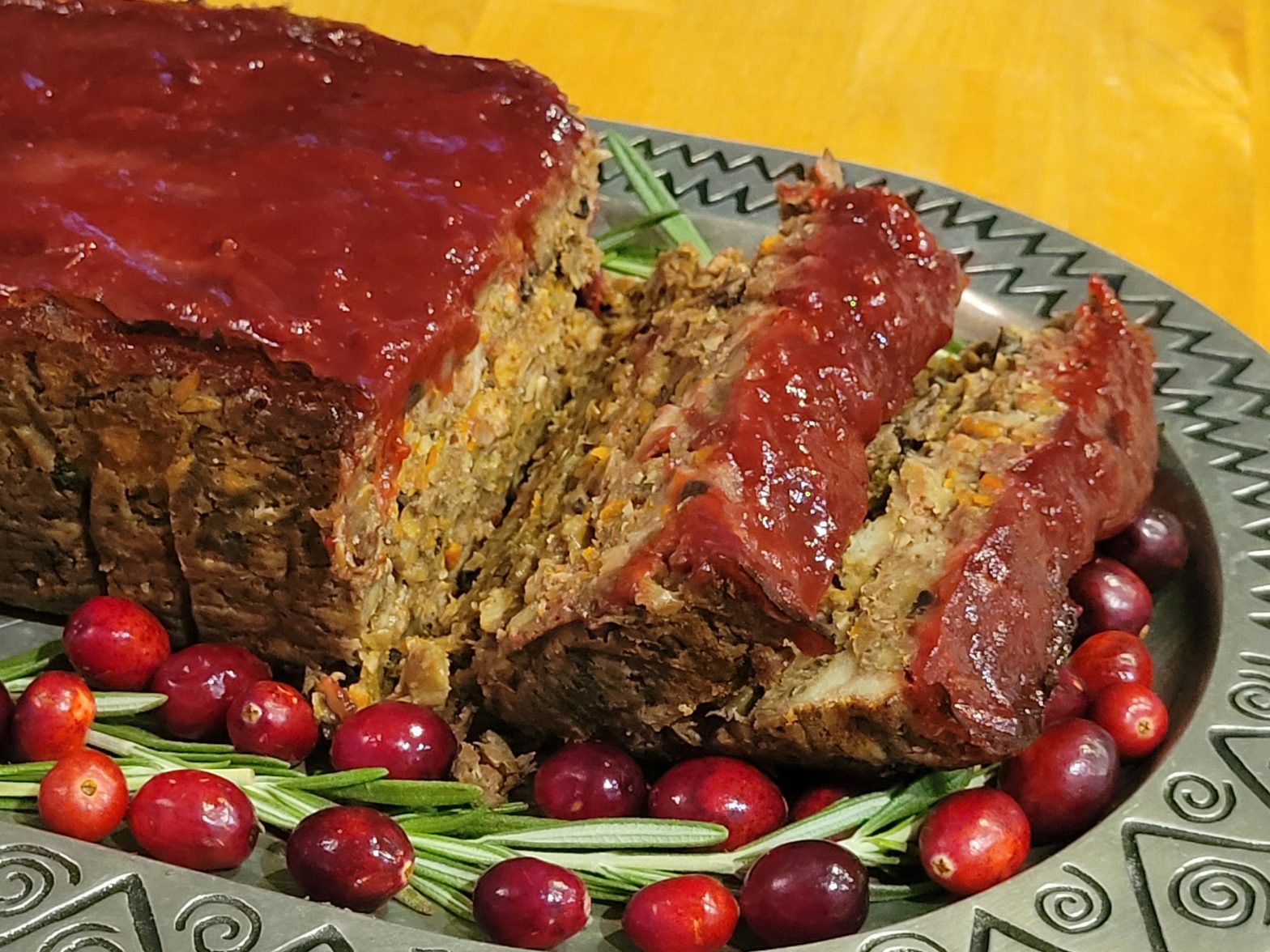 Baked lentil loaf with glaze on platter with fresh rosemary sprigs and whole cranberries