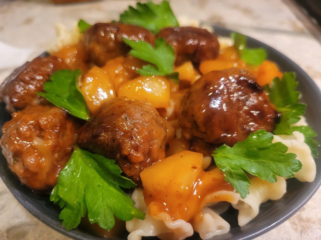 A bowl of meatballs and rice with sauce.