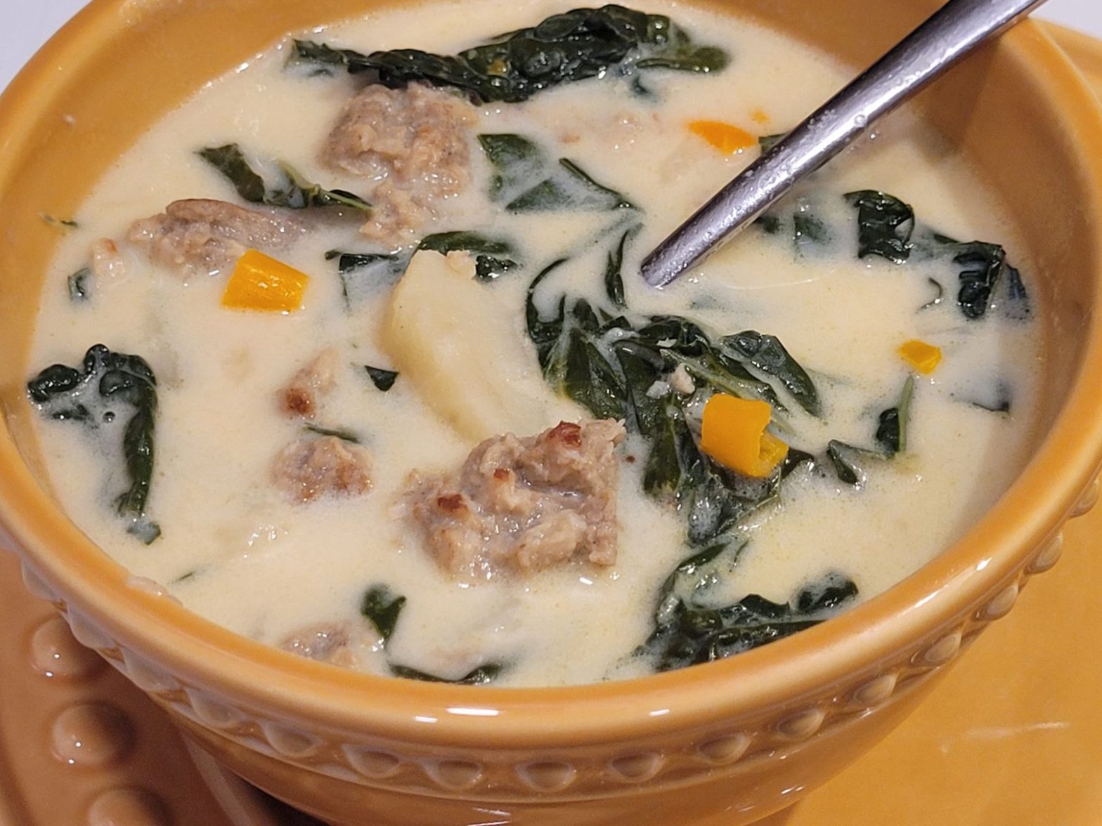 A bowl of soup with sausage and spinach.